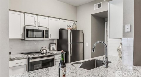 A kitchen with a black fridge, white cabinets, and a granite countertop.