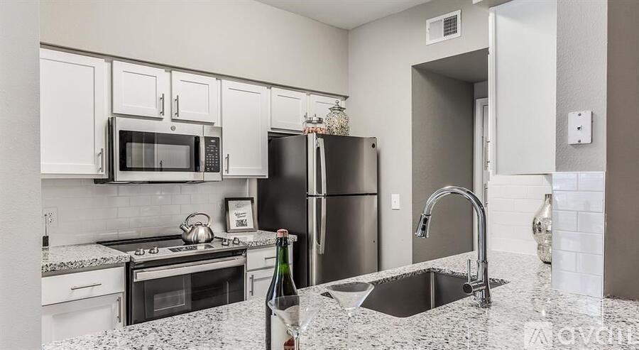 A kitchen with a black fridge, white cabinets, and a granite countertop.