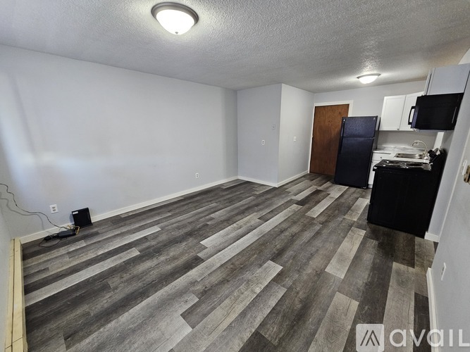 A room with wooden flooring and a black refrigerator.