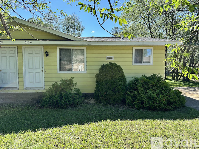 A yellow house with a white door and windows surrounded by greenery.