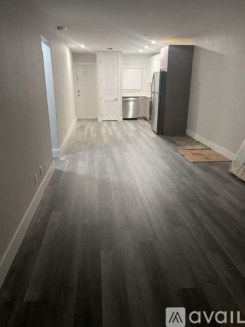 A long hallway with wood floors and a refrigerator in the corner.