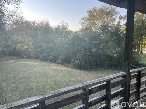 A wooden deck overlooks a grassy field with trees in the background.