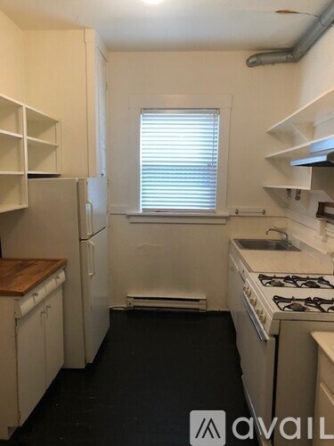 A small kitchen with white appliances and a window with blinds.