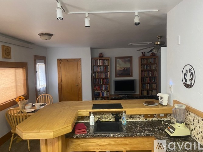 A kitchen with a wooden table and chairs, a blender on the counter, and a bookshelf filled with books.