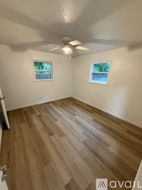 A room with wooden flooring and two windows.