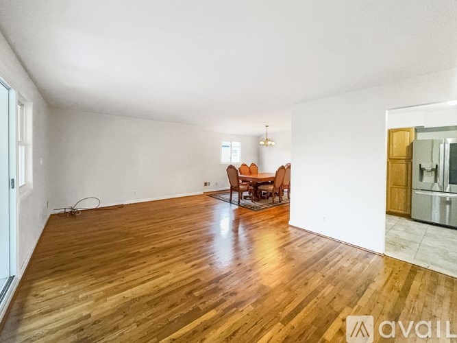 A spacious room with wooden flooring and a dining area in the background.