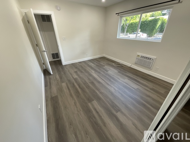 A room with a grey floor and a window showing trees outside.