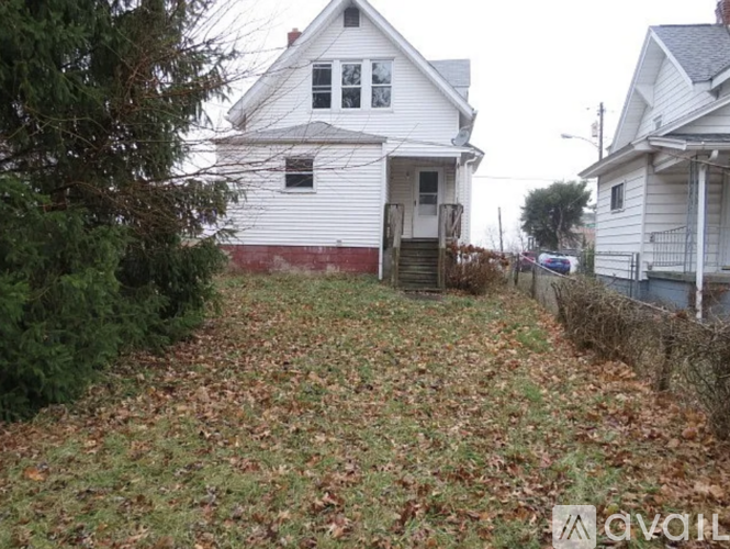 A white house with a red stripe on the side is surrounded by a grassy area with fallen leaves.