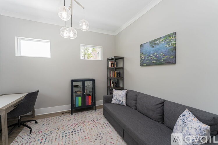 A living room with a grey couch, a desk, and a bookshelf.