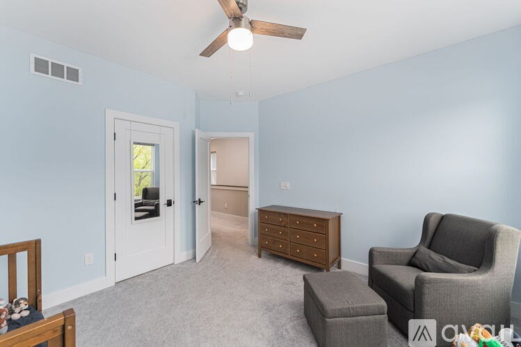 A room with a ceiling fan and a grey armchair.