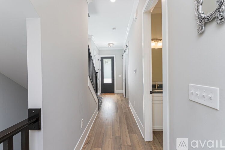 A hallway with wood floors and white walls leading to a door.