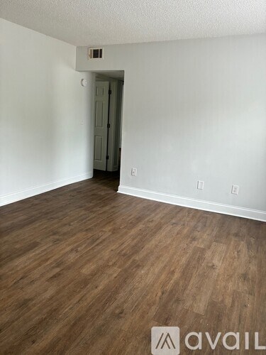A room with wooden flooring and a white wall with a doorway in the background.
