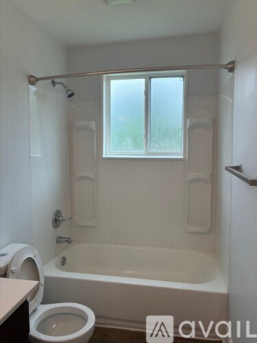 A white bathroom with a toilet, tub, and window.