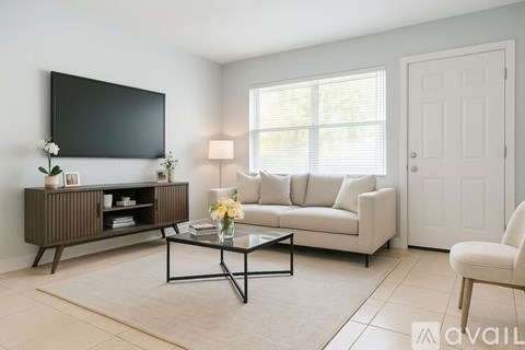 A living room with a grey rug, a white sofa, a wooden cabinet, a flat screen TV and a door.