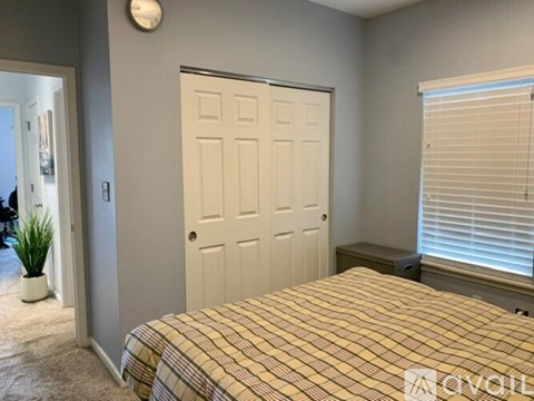 A bedroom with a bed, a door, and a window with blinds.