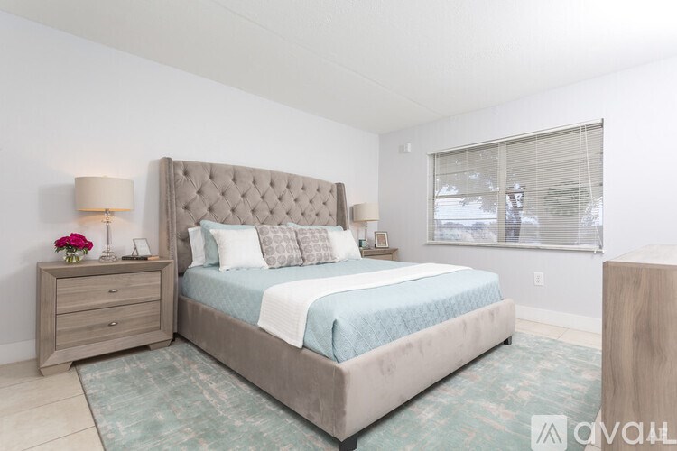 A bedroom with a large bed, a nightstand with a lamp, and a window with blinds.