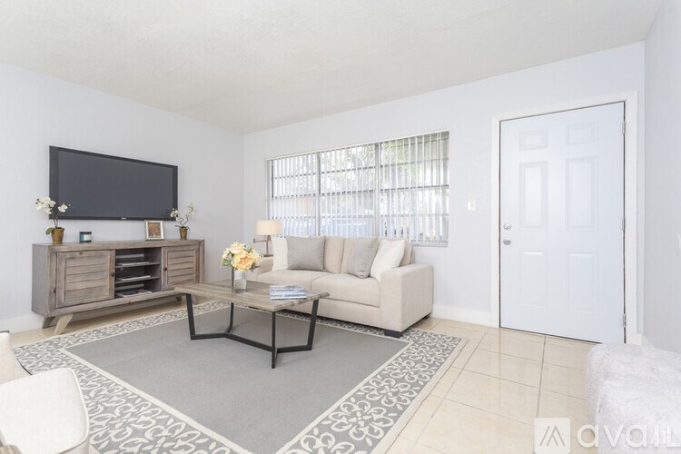 A living room with a grey rug, a white couch, a wooden cabinet, a flat screen TV and a door.