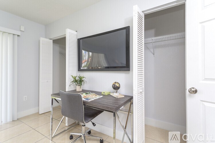 A room with a desk and a chair with a television mounted on the wall.
