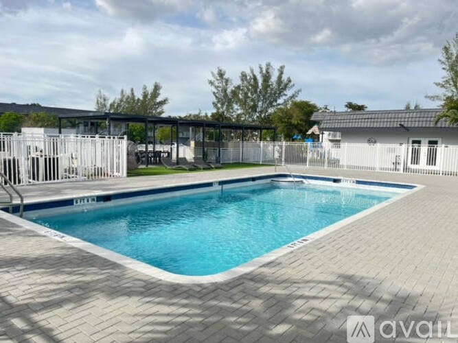 A large outdoor swimming pool surrounded by a brick patio and a white fence.
