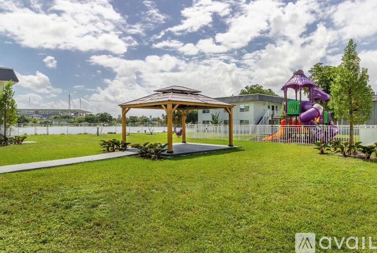 A gazebo sits in a grassy area with a playground in the background.