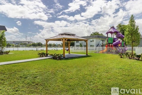 A gazebo sits in a grassy area with a playground in the background.