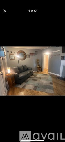 A living room with a grey couch and a round mirror on the wall.