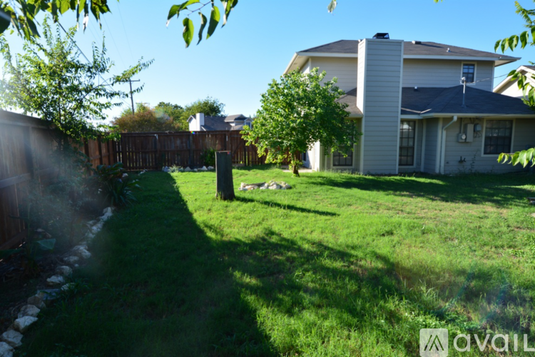 A grassy area in front of a house with a tree and a fence.