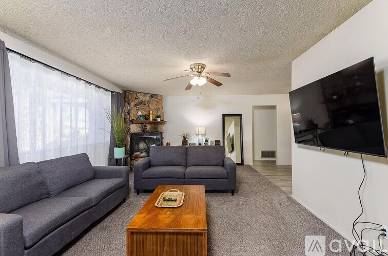 A living room with a grey couch, a wooden coffee table, and a flat screen TV mounted on the wall.