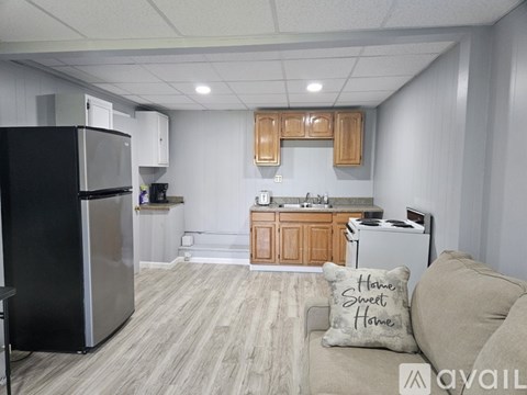 A kitchen with a black fridge, wooden cabinets, and a couch with a pillow that says "Home Sweet Home".