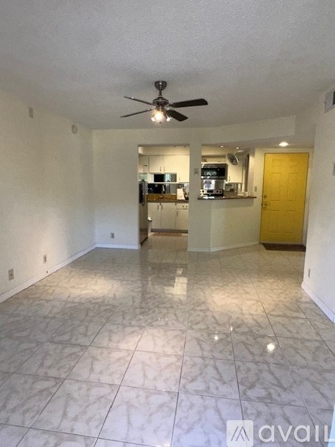 A spacious living room with a ceiling fan and a kitchen in the background.