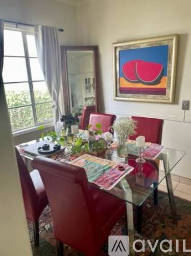 A dining room with a glass table and red chairs.