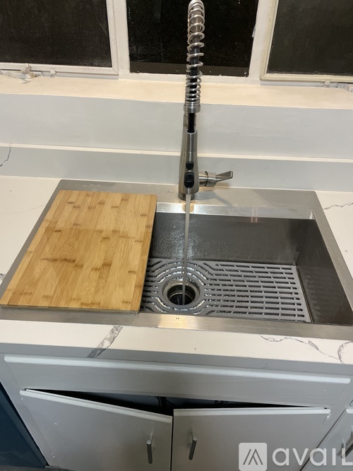 A kitchen sink with a wooden cutting board on top of it.