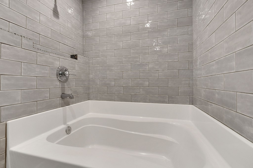 A white bathtub in a bathroom with grey tiled walls.