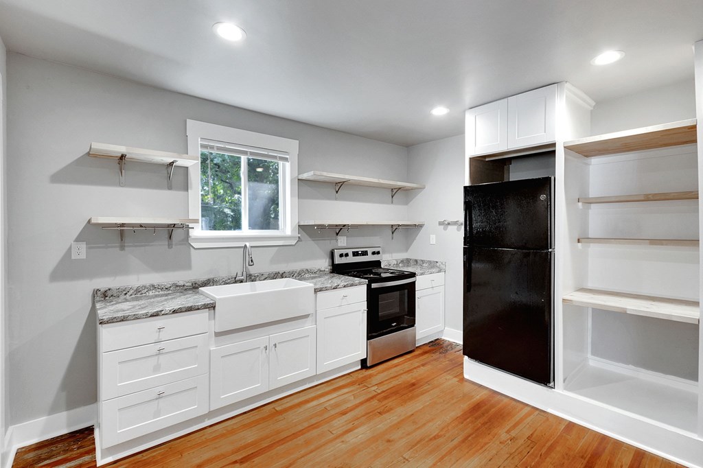 A kitchen with white cabinets and a black refrigerator.