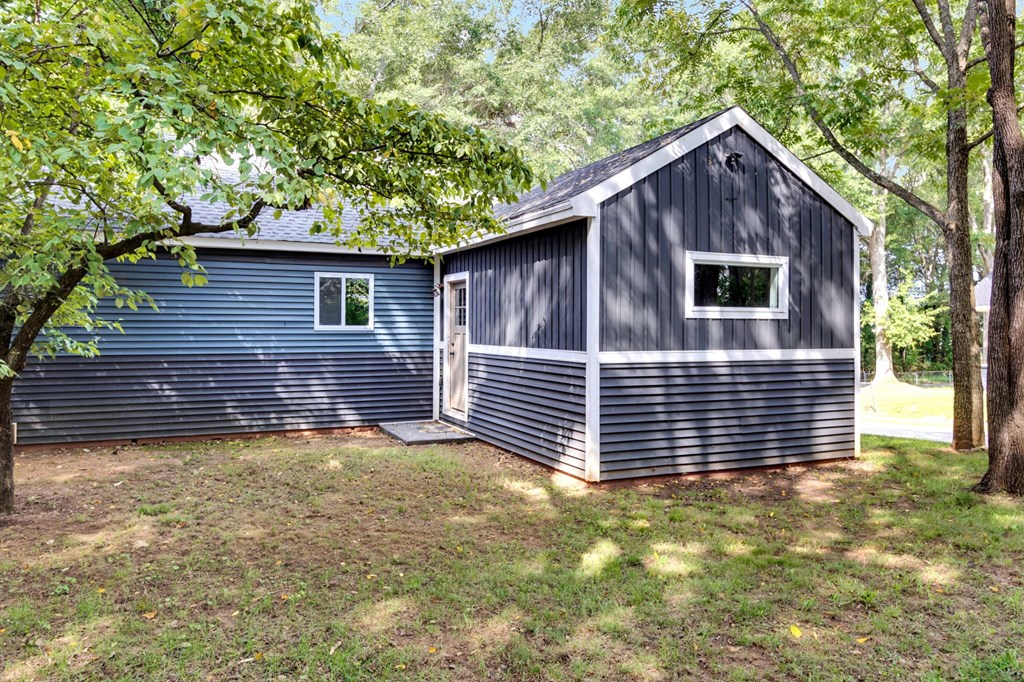 A blue shed with a white window is surrounded by trees.