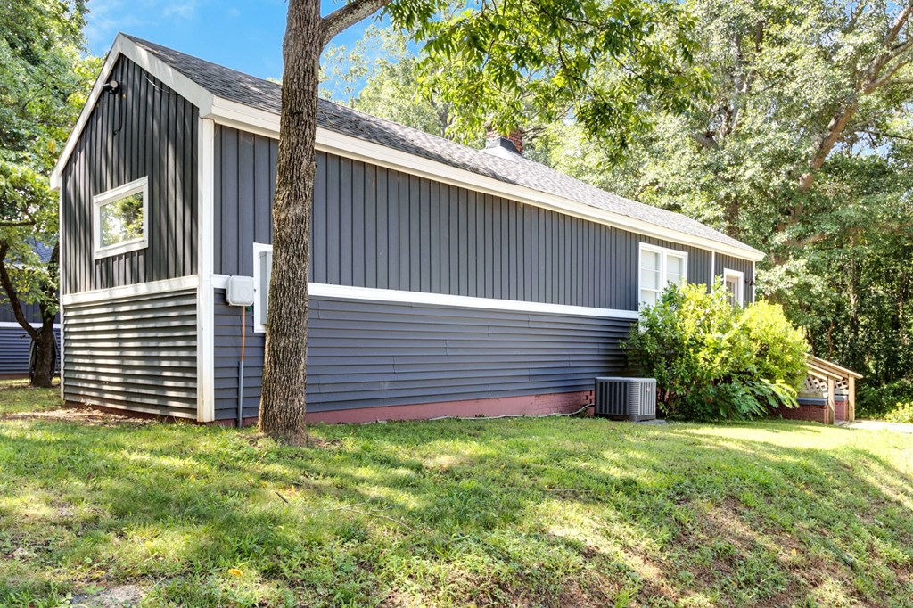 A grey barn with a red trim and a window is surrounded by greenery.