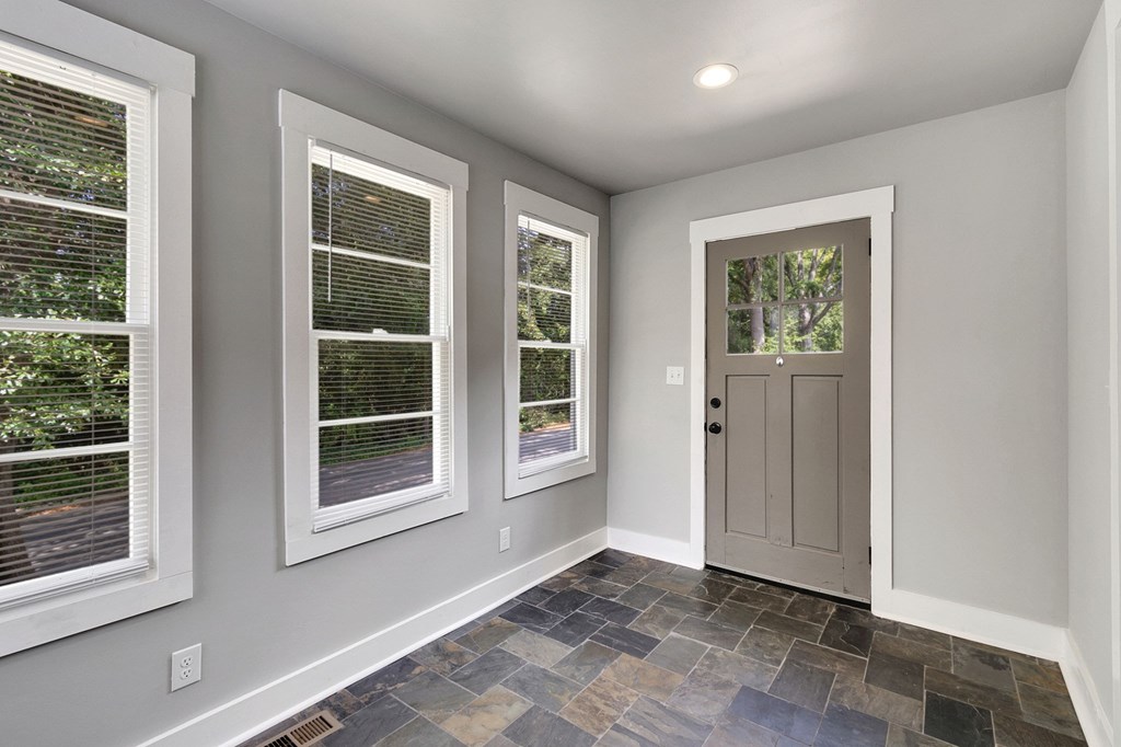 A room with a slanted ceiling, a door, and three windows.