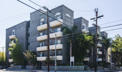A grey apartment building with balconies and trees in front.