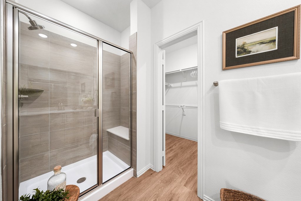 A bathroom with a walk-in shower and a white door leading to a closet.