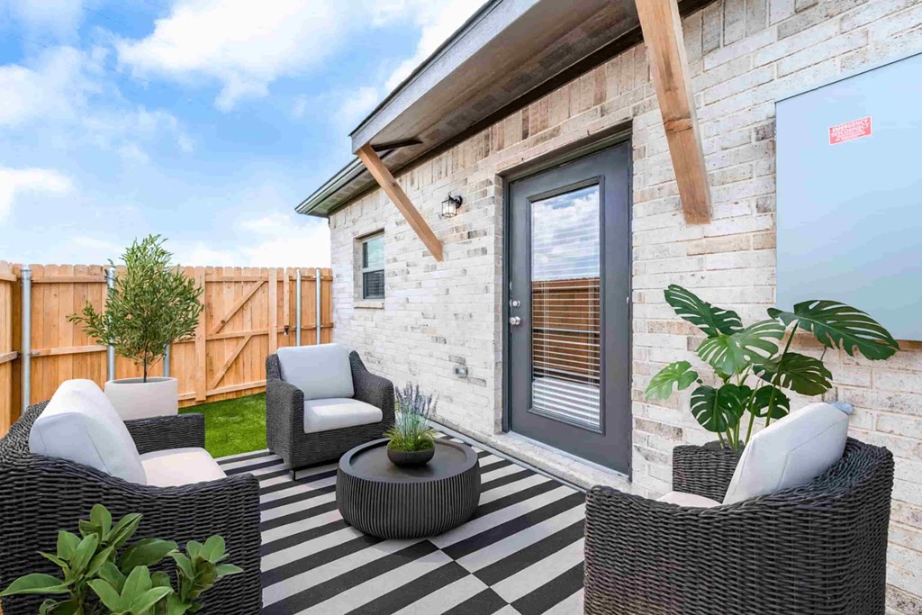A patio with a black and white striped rug, two chairs, and a table with a potted plant on it.