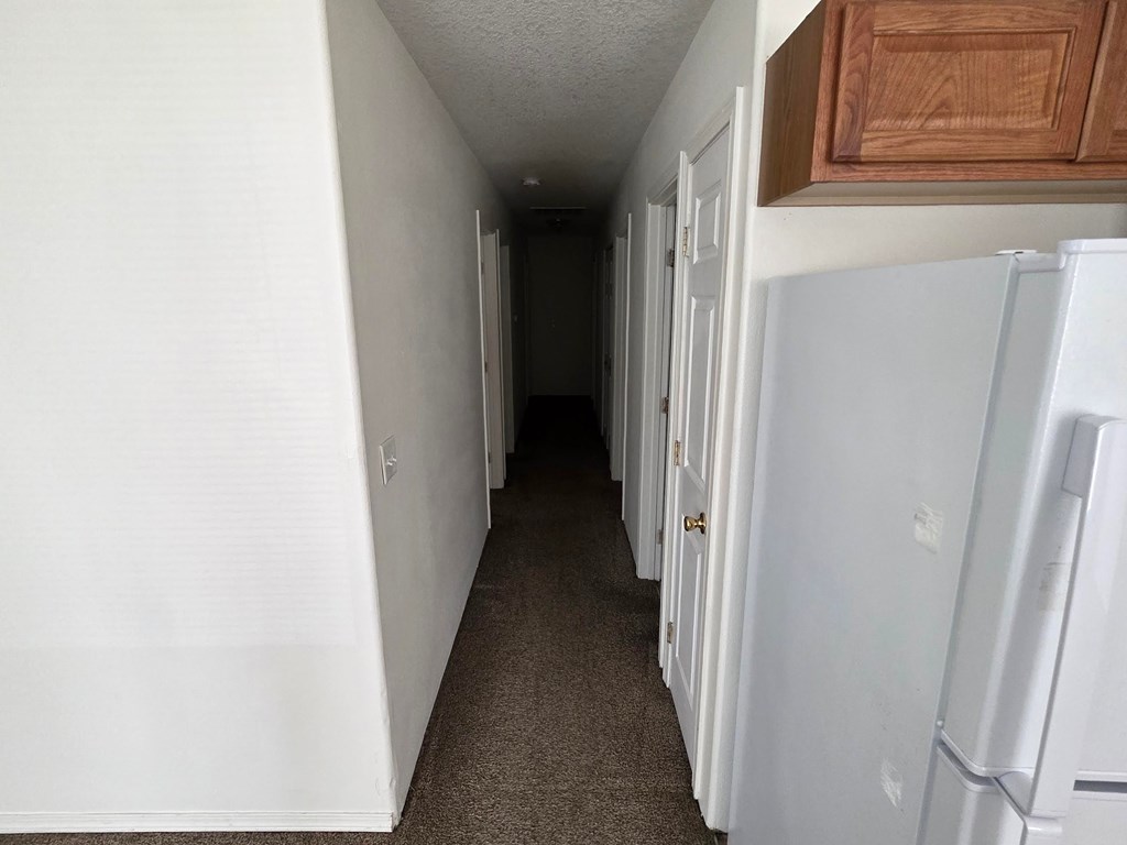 A long hallway with a white door on the right and a white wall on the left.