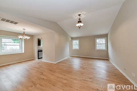 A spacious room with wooden floors and a chandelier hanging from the ceiling.