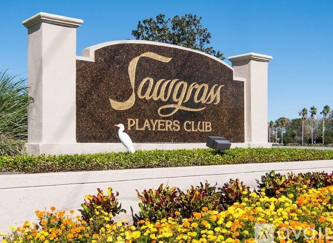 A sign for Sawgrass Players Club with a white bird statue in front.