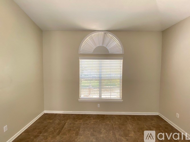 A room with a window covered by white blinds and a brown floor.