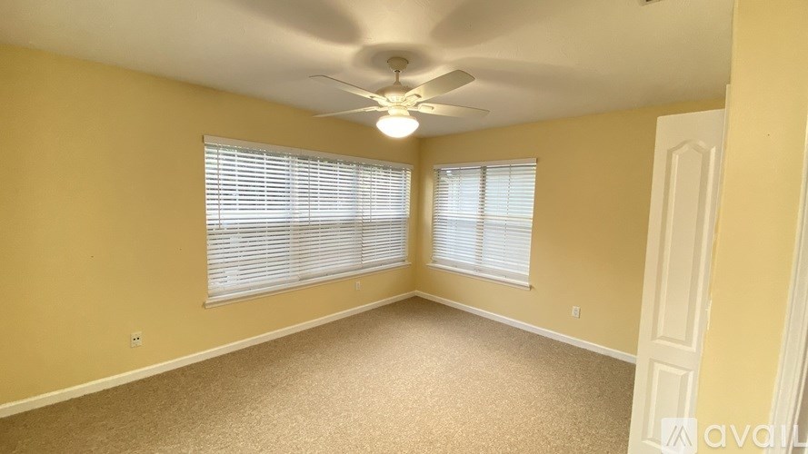 A room with a carpeted floor, a ceiling fan, and a door.