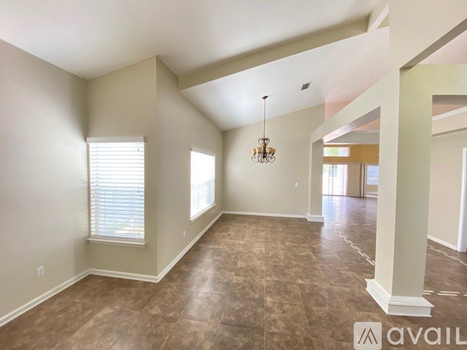 A spacious room with a chandelier and a window with blinds.