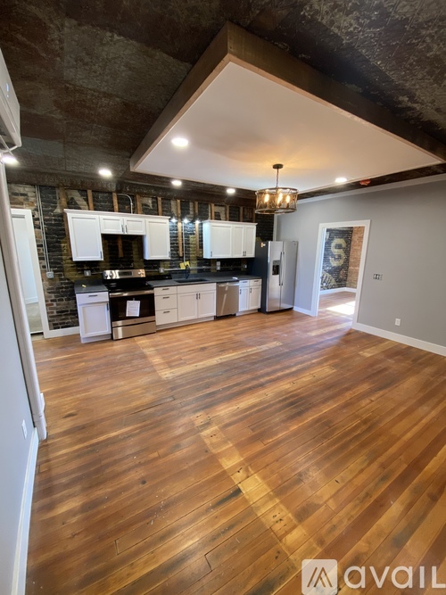A large open space with wooden floors and a kitchen area with white appliances.