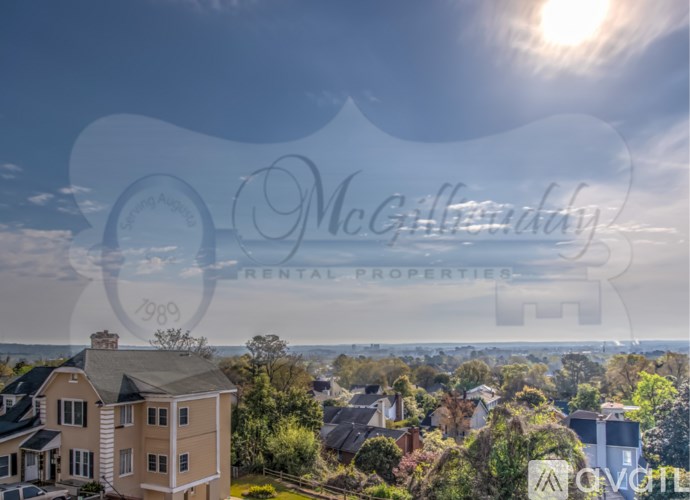 A sunny day in a neighborhood with a house in the foreground and a clear blue sky above.
