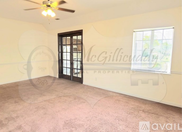 A room with a ceiling fan and a window with a view of trees.