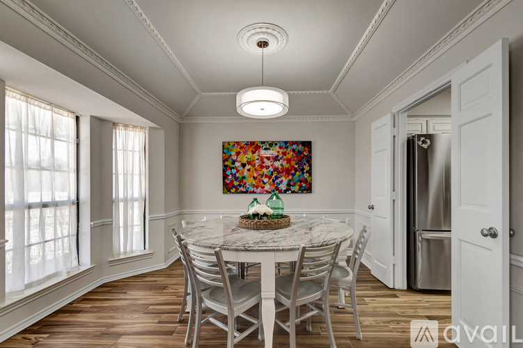 A dining room with a round table and chairs, a painting on the wall, and a refrigerator in the corner.